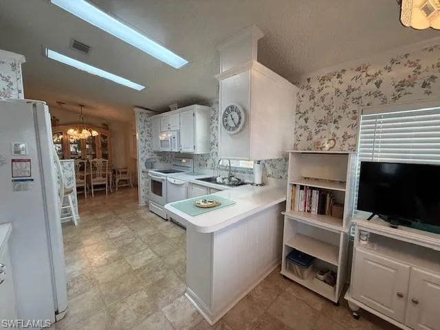 Kitchen featuring light countertops, a peninsula, white appliances, a sink, and an inviting chandelier