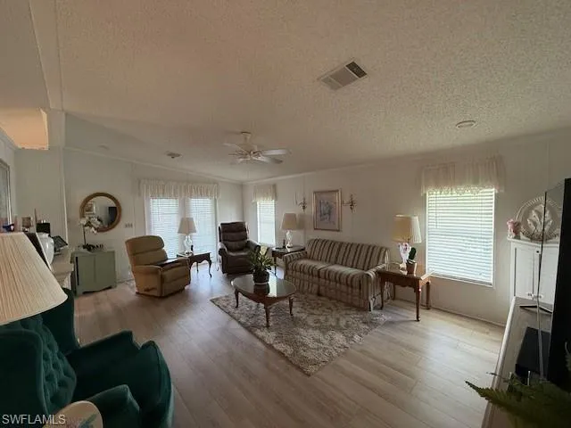 Living room with visible vents, crown molding, wood finished floors, and ceiling fan