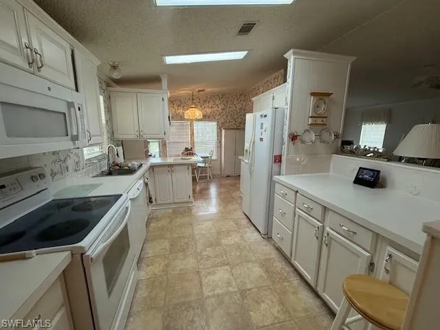 Kitchen with white appliances, wallpapered walls, a sink, visible vents, and a peninsula