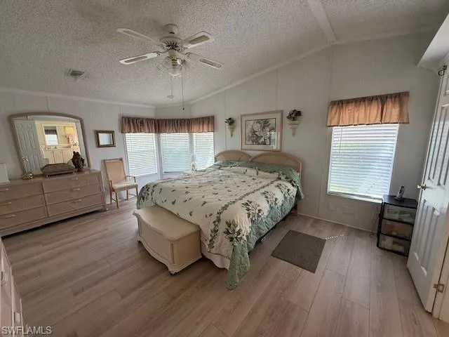 Bedroom featuring a textured ceiling, visible vents, vaulted ceiling, and light wood finished floors