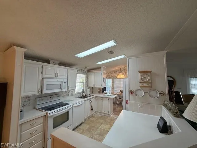 Kitchen with lofted ceiling, white appliances, a sink, visible vents, and white cabinets