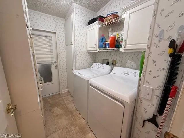 Laundry room with crown molding, separate washer and dryer, a textured ceiling, wallpapered walls, and cabinet space