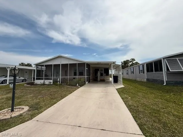 Manufactured / mobile home with a sunroom, an attached carport, concrete driveway, and a front lawn