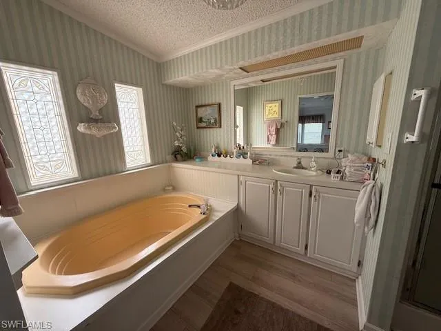 Full bath with vanity, crown molding, a textured ceiling, wallpapered walls, and a garden tub