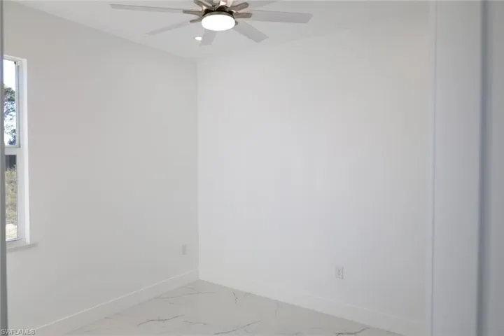 Empty room featuring light marble finish floors and ceiling fan