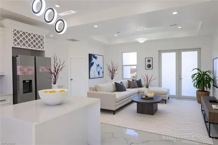 Living area featuring a tray ceiling, light marble finish floors, recessed lighting, and french doors