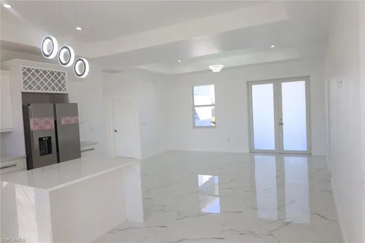 Kitchen with white cabinetry, stainless steel refrigerator with ice dispenser, light marble finish floors, a raised ceiling, and recessed lighting