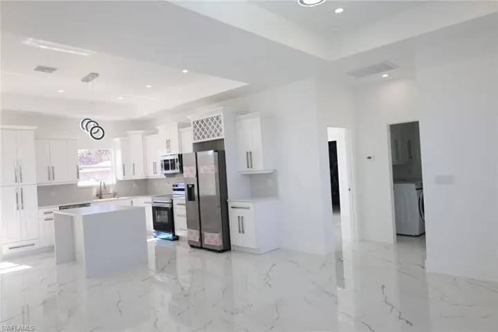 Kitchen with a raised ceiling, a center island, hanging light fixtures, appliances with stainless steel finishes, and light marble finish floors