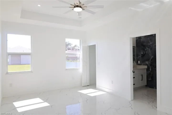 Unfurnished bedroom featuring light marble finish flooring, ceiling fan, a raised ceiling, and recessed lighting