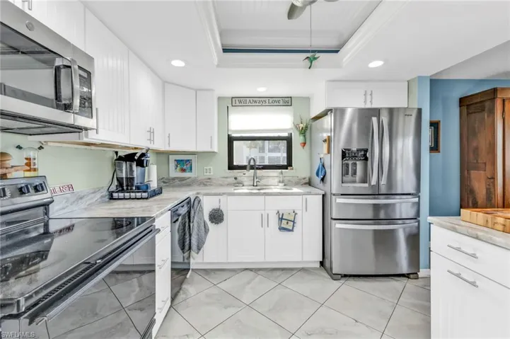 Kitchen featuring crown molding, a raised ceiling, appliances with stainless steel finishes, white cabinets, and a sink