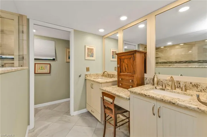 Full bath featuring tiled shower, two vanities, and a sink