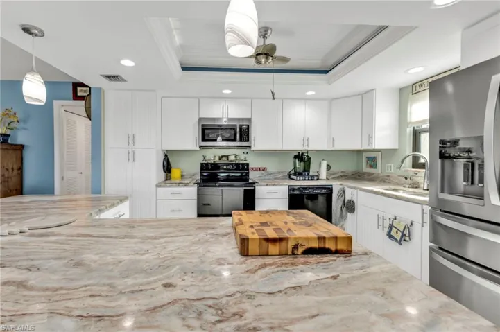 Kitchen with light stone counters, a raised ceiling, a sink, and black appliances