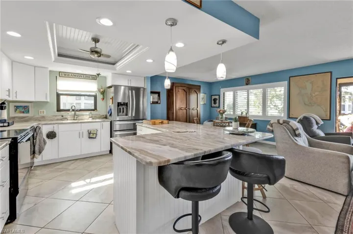 Kitchen with stainless steel fridge, a raised ceiling, open floor plan, black electric range, and light tile patterned flooring
