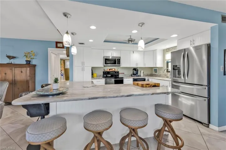 Kitchen featuring white cabinets, appliances with stainless steel finishes, light stone countertops, a tray ceiling, and a sink