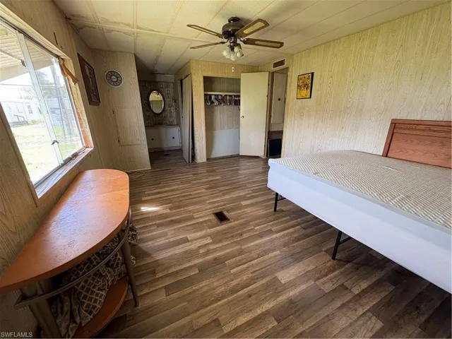 Bedroom with wooden walls, dark wood-style floors, a closet, and ceiling fan