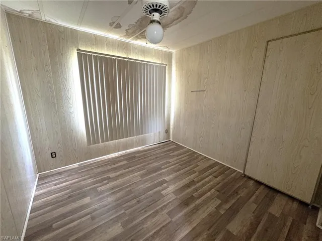 Unfurnished bedroom featuring dark wood-type flooring, ceiling fan, and wood walls