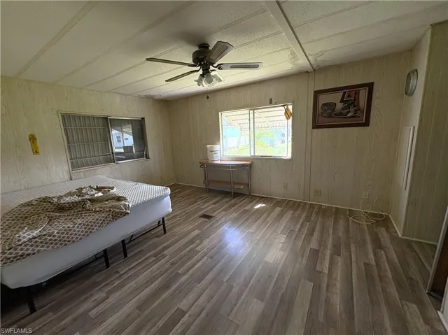 Bedroom with dark wood-style flooring, a ceiling fan, wooden walls, and beam ceiling