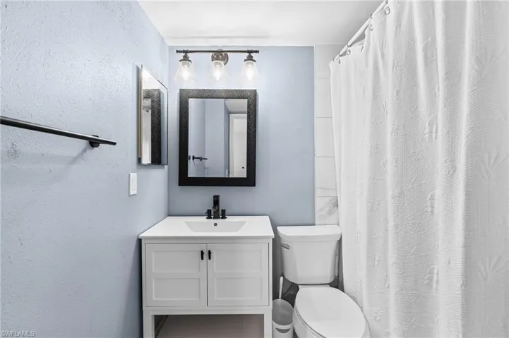 Bathroom with toilet, vanity, shower/ tub, and a textured wall