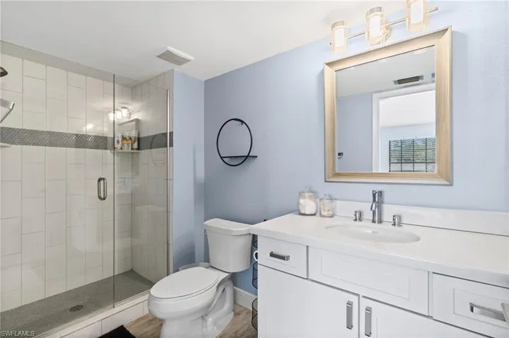 Bathroom featuring vanity, wood finished floors, visible vents, a shower stall, and toilet