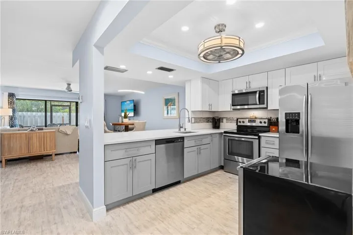 Kitchen with visible vents, gray cabinets, a sink, appliances with stainless steel finishes, and a raised ceiling