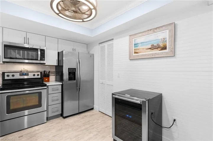 Kitchen with wine cooler, a tray ceiling, stainless steel appliances, light wood-style floors, and crown molding