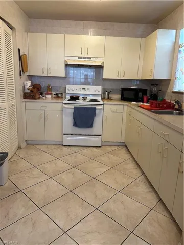Kitchen with electric stove, exhaust hood, backsplash, and light tile floors