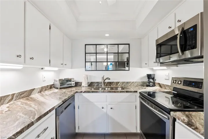 Galley kitchen featuring white cabinetry, stone-finish countertops, and stainless steel appliances