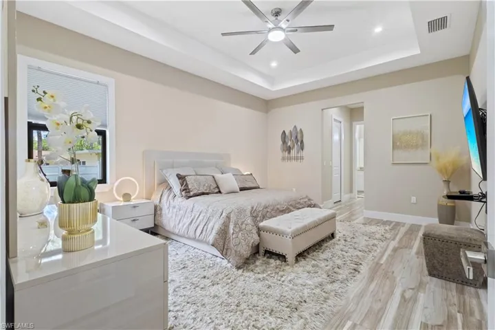 Bedroom featuring a tray ceiling with recessed lighting and a ceiling fan, wood-finish flooring, and a window with blinds