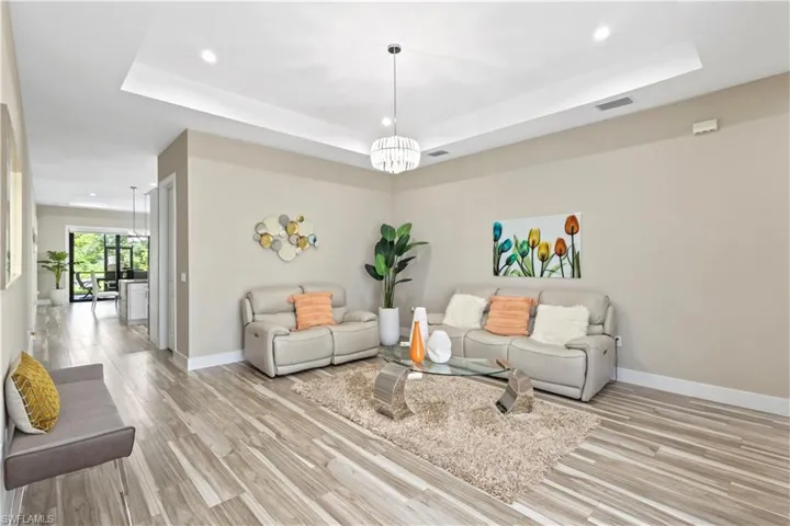 Spacious living area featuring wood-finish flooring, recessed lighting, and a tray ceiling with a central chandelier