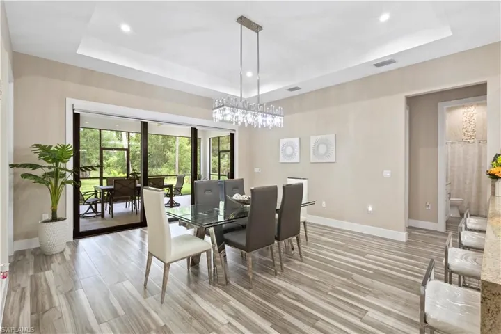 Spacious dining area featuring wood-finish flooring, a tray ceiling with recessed lighting, and a contemporary crystal chandelier