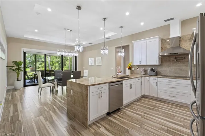 Open-concept kitchen featuring wood-finish flooring, white cabinetry, a stone-wrapped island with a built-in sink, stainless steel appliances, and a full-height stone backsplash