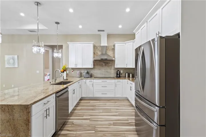 Spacious kitchen featuring an extended island with stone countertop, white shaker cabinetry, stainless steel appliances, and wood-finish flooring