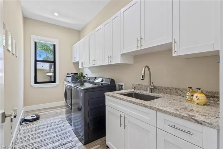 Laundry room featuring a utility sink, light-toned countertop, white cabinetry with silver hardware, and wood-finish flooring