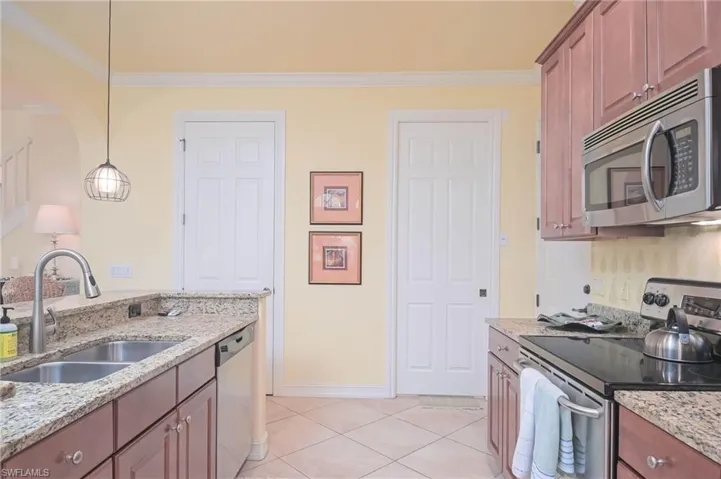 Kitchen with ornamental molding, stainless steel appliances, hanging light fixtures, and sink