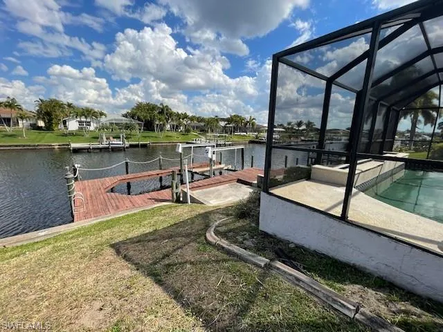Dock featuring glass enclosure, a sunroom, a water view, an outdoor pool, and boat lift