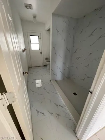 Full bath with a marble finish shower and light marble finish flooring