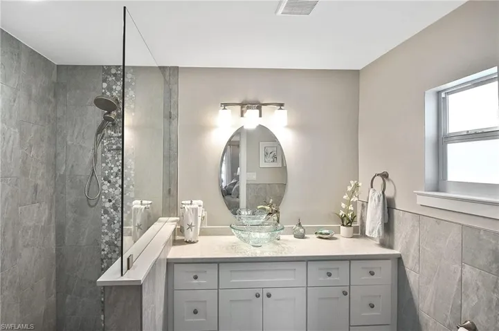 Bathroom with tile walls, a wainscoted wall, visible vents, walk in shower, and vanity