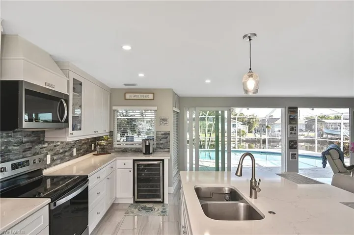 Kitchen featuring wine cooler, backsplash, a sink, stainless steel appliances, and white cabinets