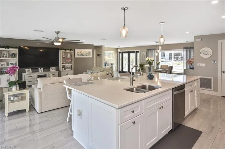 Kitchen featuring stainless steel dishwasher, open floor plan, white cabinets, and a sink