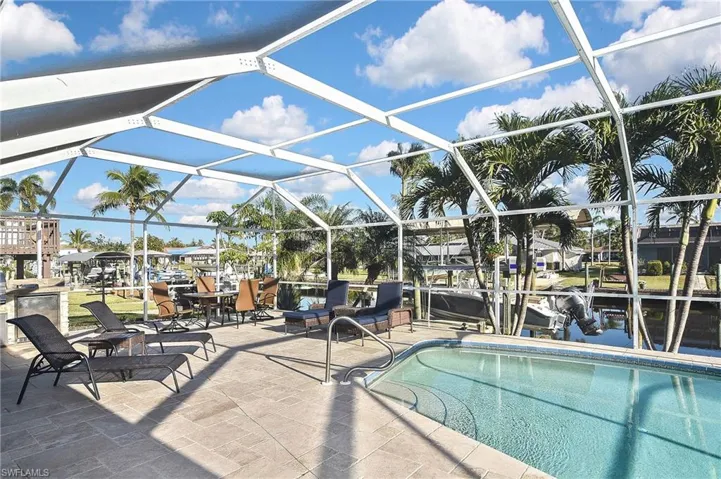 Outdoor pool with glass enclosure, boat lift, a patio area, and a boat dock