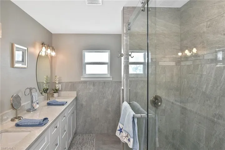 Bathroom with a stall shower, double vanity, tile walls, and a wainscoted wall