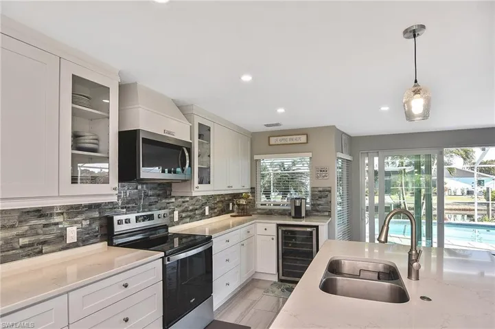Kitchen featuring a sink, beverage cooler, stainless steel appliances, white cabinets, and decorative backsplash