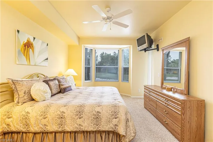 Primary carpeted bedroom with ceiling fan and multiple windows