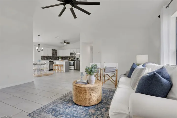 Living room with light tile patterned floors, a chandelier, ceiling fan, and lofted ceiling