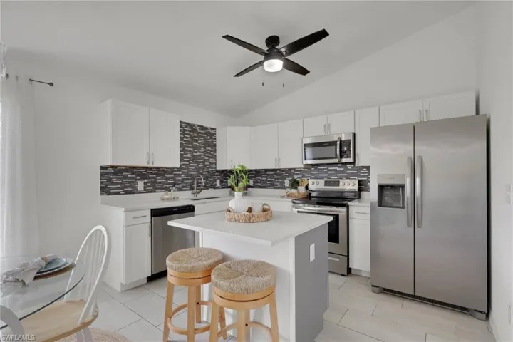 Kitchen featuring stainless steel appliances, lofted ceiling, ceiling fan, a kitchen bar, and a kitchen island