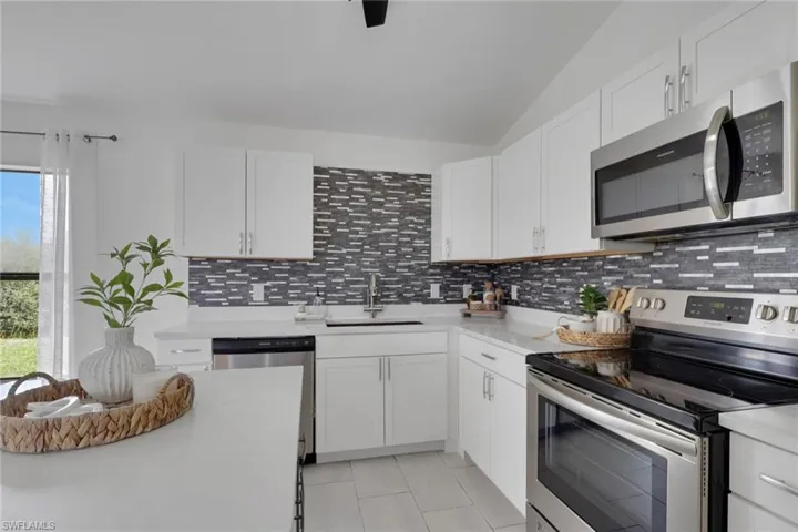 Kitchen featuring stainless steel appliances, white cabinetry, backsplash, and light stone countertops