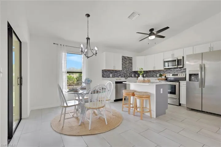 Kitchen with stainless steel appliances, a kitchen island, white cabinets, ceiling fan, and lofted ceiling