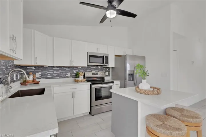 Kitchen featuring vaulted ceiling, a kitchen bar, stainless steel appliances, white cabinetry, and a center island