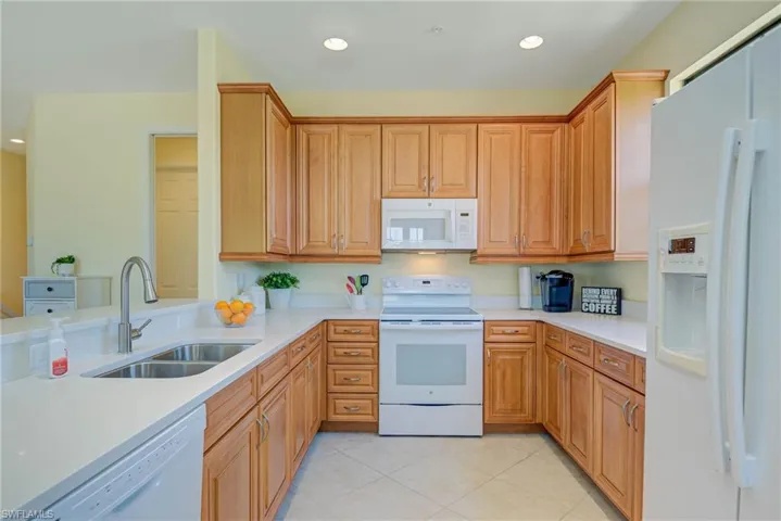 Kitchen with white appliances, recessed lighting, light tile patterned floors, light stone counters, and brown cabinets