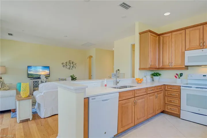 Kitchen featuring white appliances, open floor plan, a peninsula, brown cabinetry, and recessed lighting